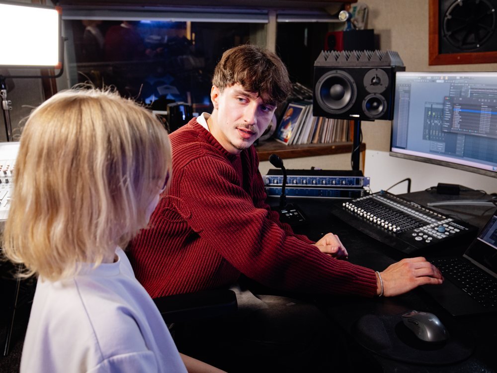 A producer at the mixing desk talking with a young singer